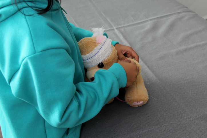 4-year-old brunette Latina girl with glasses represents mistreatment and physical abuse in her teddy bear with bandages on her head, she cares for him and heals his wounds
